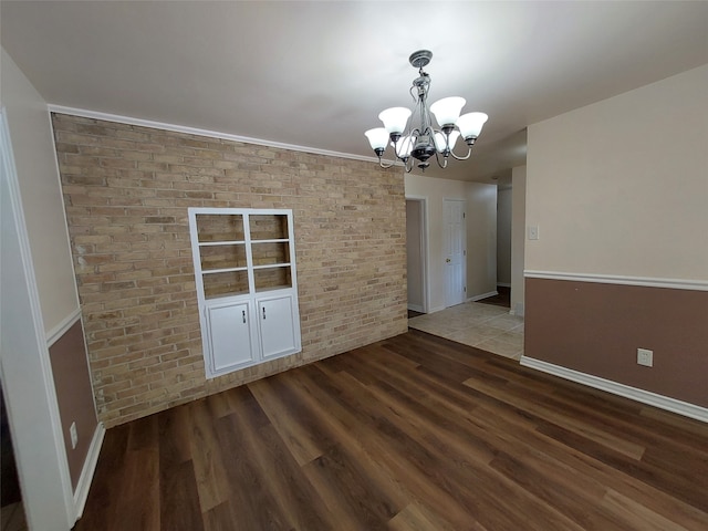 unfurnished dining area featuring a chandelier, hardwood / wood-style flooring, crown molding, and brick wall