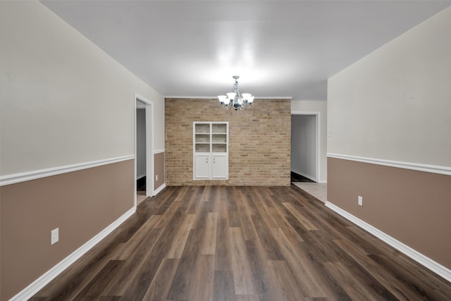 unfurnished dining area with a notable chandelier, dark wood-type flooring, and brick wall