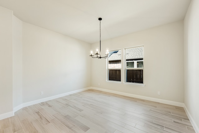 spare room with a chandelier and light wood-type flooring