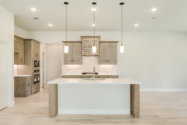 kitchen featuring appliances with stainless steel finishes, a center island with sink, decorative light fixtures, and light hardwood / wood-style flooring