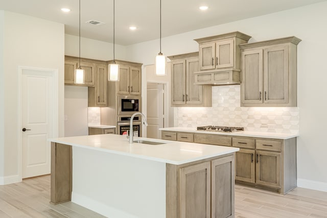 kitchen with stainless steel appliances, light hardwood / wood-style floors, a center island with sink, and sink