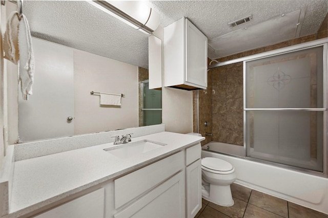 full bathroom featuring vanity, bath / shower combo with glass door, tile patterned flooring, toilet, and a textured ceiling