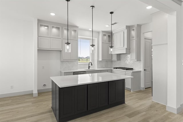 kitchen with sink, backsplash, a center island, decorative light fixtures, and light wood-type flooring