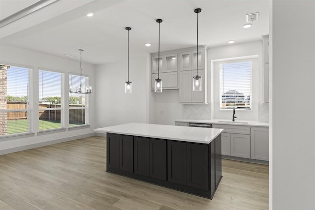 kitchen featuring a kitchen island, tasteful backsplash, sink, hanging light fixtures, and light hardwood / wood-style floors