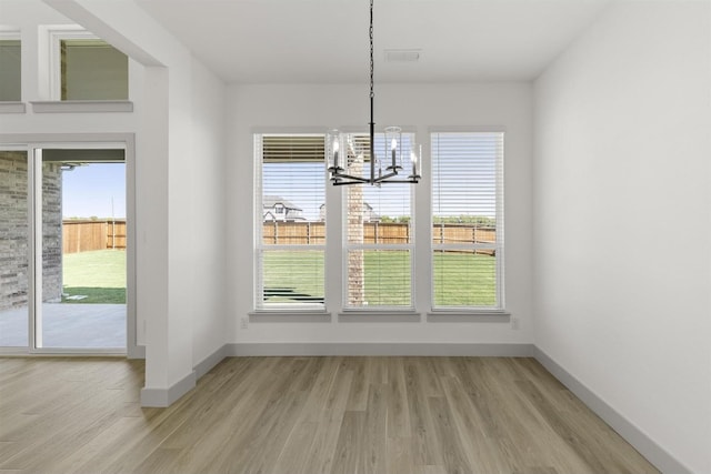 unfurnished dining area with an inviting chandelier and light wood-type flooring