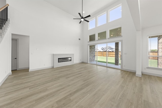 unfurnished living room featuring ceiling fan, a towering ceiling, and light wood-type flooring