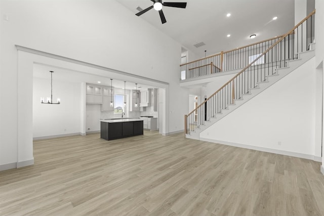 unfurnished living room featuring sink, a towering ceiling, ceiling fan with notable chandelier, and light wood-type flooring