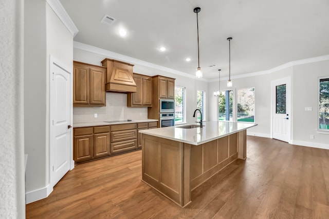 kitchen featuring stainless steel appliances, custom exhaust hood, an island with sink, hardwood / wood-style floors, and pendant lighting