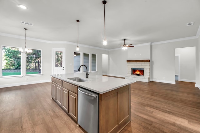 kitchen with a stone fireplace, hardwood / wood-style floors, sink, an island with sink, and stainless steel dishwasher