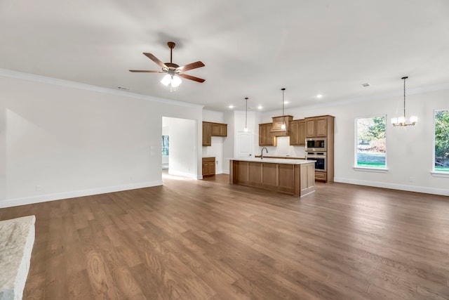 kitchen featuring dark wood-type flooring, appliances with stainless steel finishes, decorative light fixtures, and an island with sink