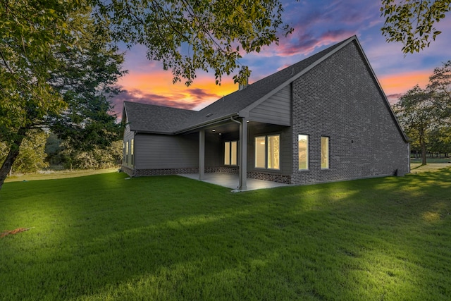 back house at dusk with a patio area and a yard