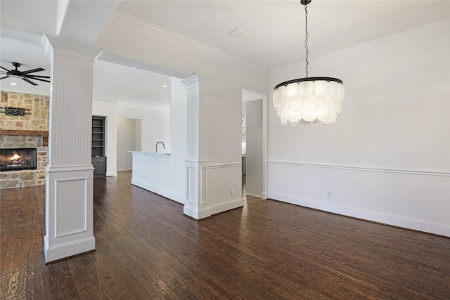 unfurnished dining area with ornate columns, dark hardwood / wood-style flooring, ceiling fan with notable chandelier, and a stone fireplace