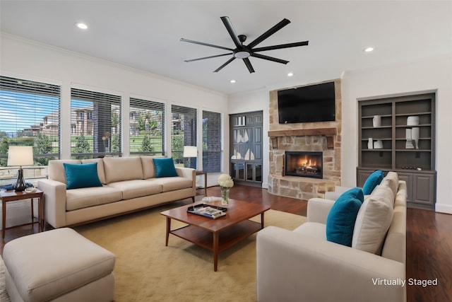 living room featuring built in features, hardwood / wood-style floors, a fireplace, ceiling fan, and ornamental molding