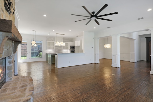 unfurnished living room with ornate columns, dark hardwood / wood-style flooring, a stone fireplace, and ceiling fan