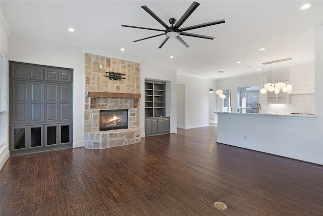 unfurnished living room featuring a stone fireplace, crown molding, dark hardwood / wood-style floors, and ceiling fan