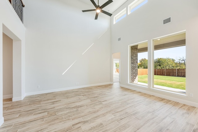 unfurnished living room with ceiling fan, a towering ceiling, baseboards, and light wood-type flooring