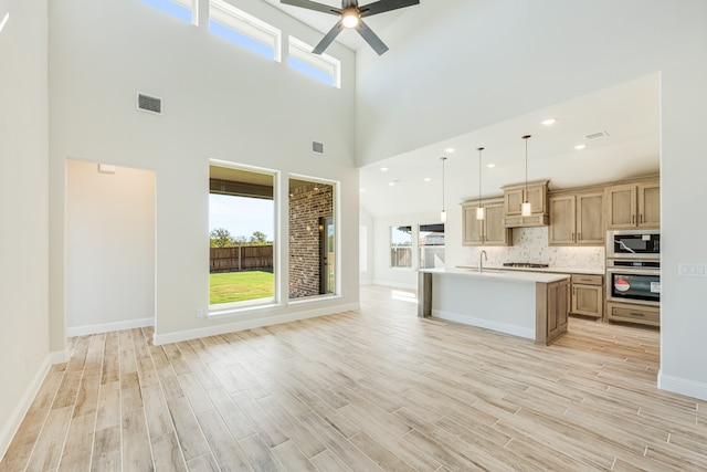 kitchen featuring light hardwood / wood-style flooring, decorative light fixtures, a center island with sink, and stainless steel appliances