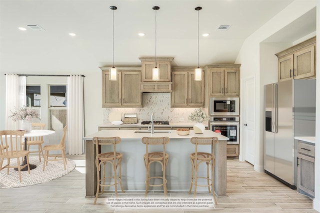 kitchen with a kitchen bar, stainless steel appliances, a center island with sink, pendant lighting, and light wood-type flooring