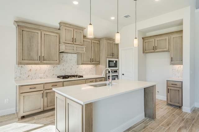 kitchen featuring stainless steel appliances, sink, an island with sink, light hardwood / wood-style flooring, and decorative light fixtures