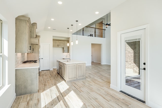 kitchen featuring a kitchen island with sink, light brown cabinets, hanging light fixtures, sink, and light hardwood / wood-style flooring