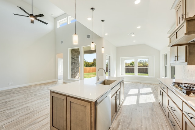 kitchen featuring light wood-type flooring, appliances with stainless steel finishes, decorative light fixtures, sink, and a kitchen island with sink