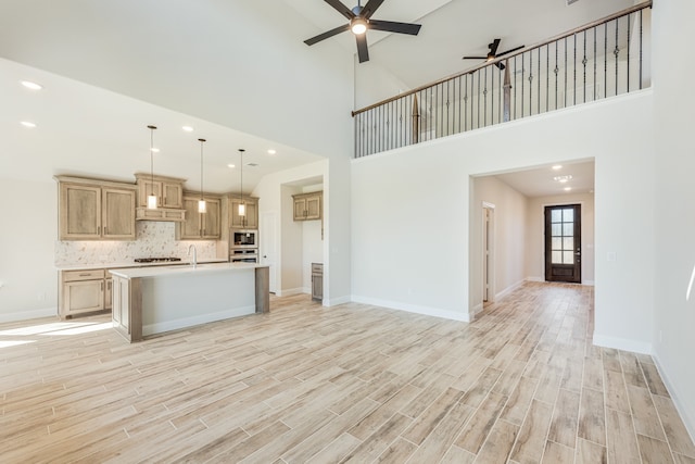 kitchen featuring stainless steel appliances, light hardwood / wood-style flooring, pendant lighting, ceiling fan, and a kitchen island with sink