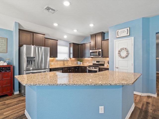 kitchen with a center island, backsplash, sink, light stone countertops, and stainless steel appliances