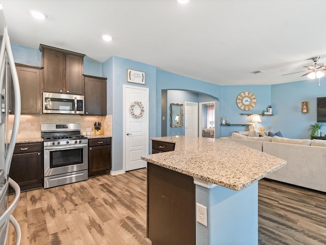 kitchen with hardwood / wood-style flooring, decorative backsplash, appliances with stainless steel finishes, a kitchen island, and dark brown cabinetry