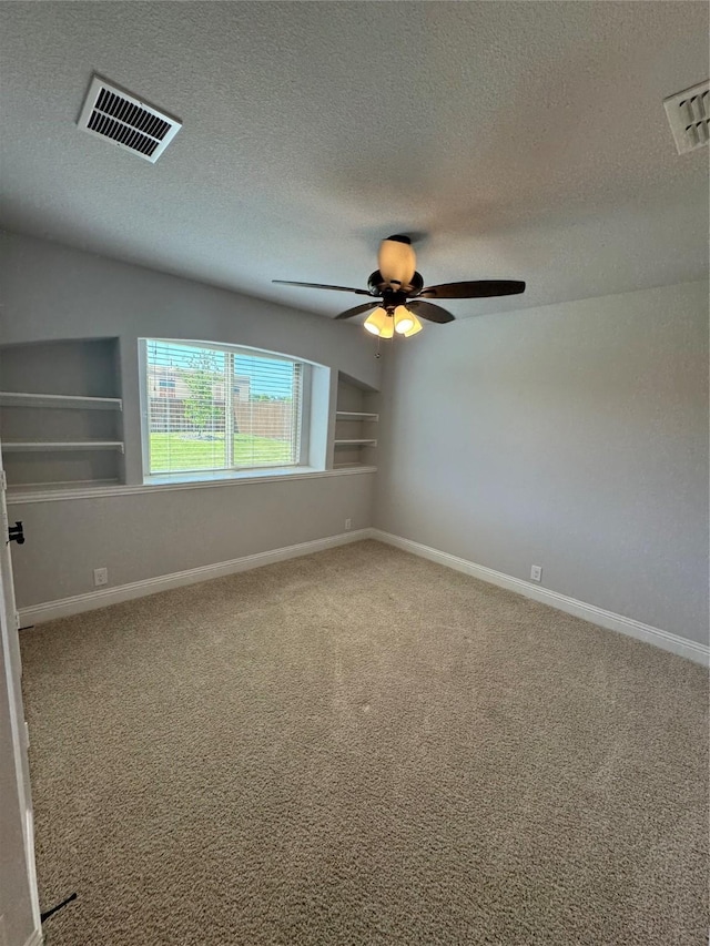 spare room with carpet, ceiling fan, a textured ceiling, and built in shelves