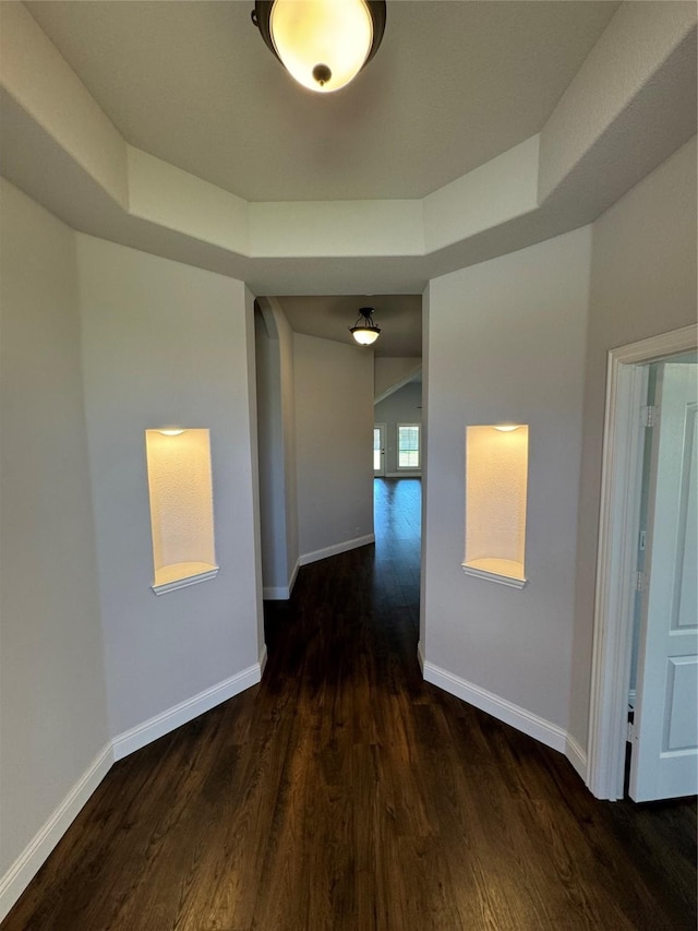 corridor with a tray ceiling and dark hardwood / wood-style floors