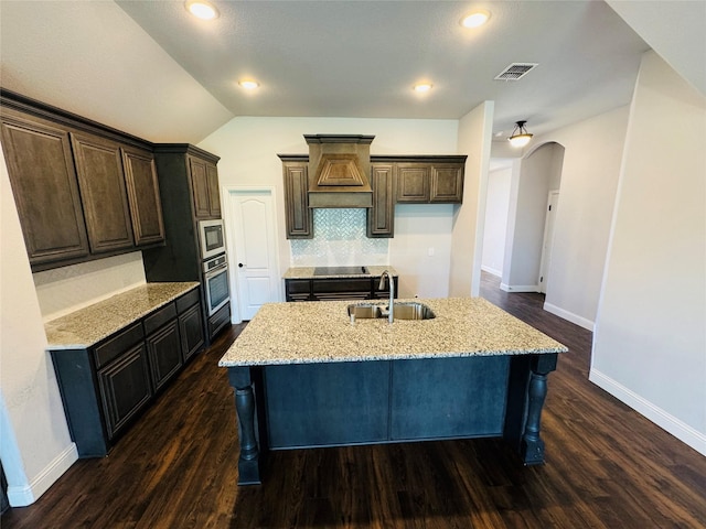 kitchen with a kitchen island with sink, sink, stainless steel oven, and lofted ceiling