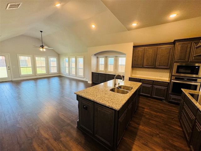 kitchen featuring built in microwave, stainless steel oven, sink, vaulted ceiling, and a kitchen island with sink