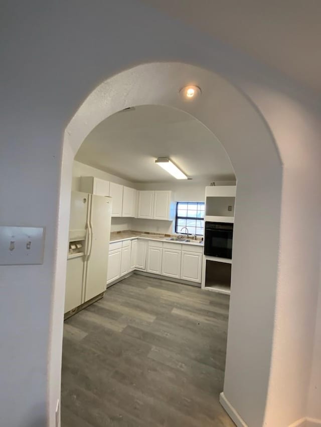 kitchen with sink, white cabinetry, white fridge with ice dispenser, hardwood / wood-style flooring, and oven