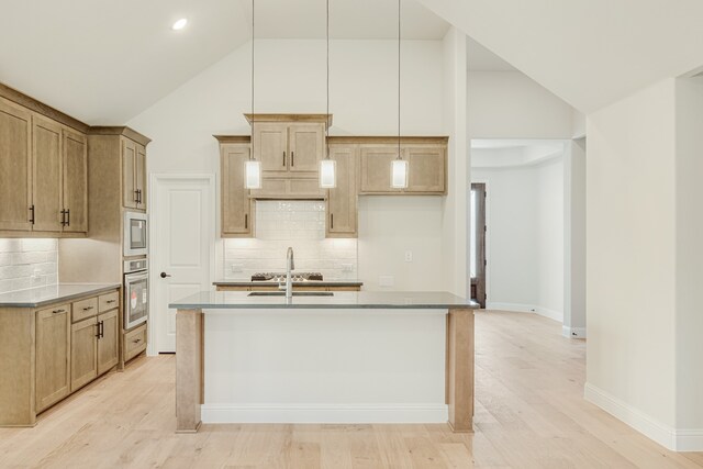 kitchen with tasteful backsplash, appliances with stainless steel finishes, light hardwood / wood-style floors, pendant lighting, and a center island with sink