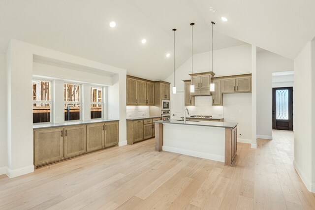 kitchen featuring tasteful backsplash, hanging light fixtures, a kitchen island with sink, high vaulted ceiling, and light wood-type flooring