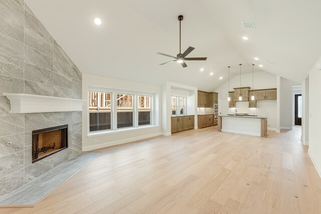 unfurnished living room featuring ceiling fan, lofted ceiling, light hardwood / wood-style flooring, and a tile fireplace