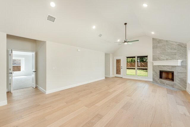 unfurnished living room with vaulted ceiling, a tile fireplace, light wood-type flooring, and ceiling fan