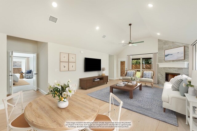 living room featuring light hardwood / wood-style flooring, ceiling fan, a premium fireplace, and vaulted ceiling