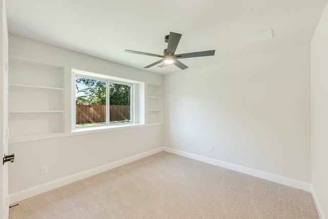 carpeted empty room with ceiling fan and built in shelves