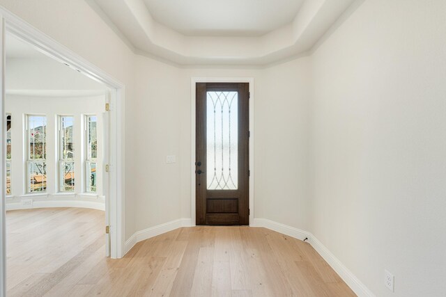 foyer featuring baseboards, light wood finished floors, and a tray ceiling