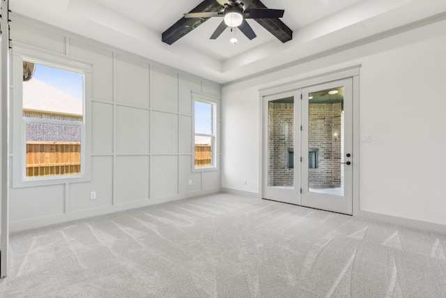 empty room with beam ceiling, a wealth of natural light, light colored carpet, and a raised ceiling