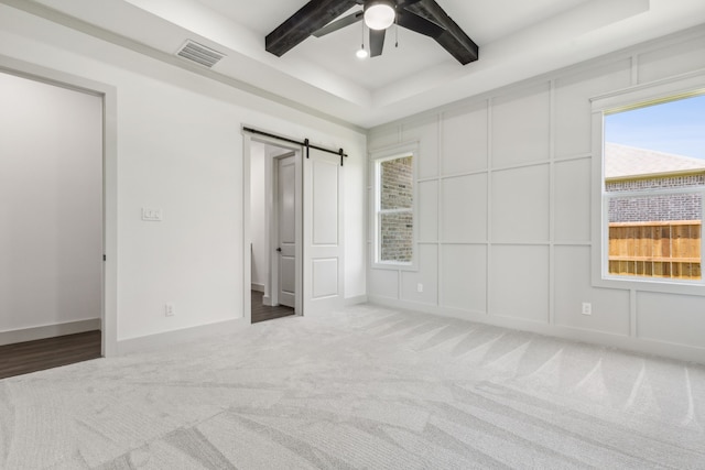 unfurnished bedroom featuring carpet floors, ceiling fan, a raised ceiling, a barn door, and beam ceiling