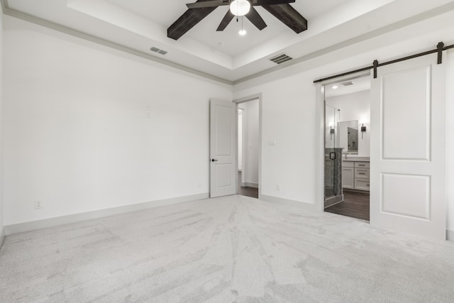 unfurnished bedroom featuring connected bathroom, beamed ceiling, carpet flooring, a raised ceiling, and a barn door