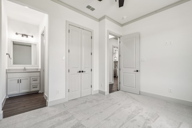 unfurnished bedroom with ensuite bathroom, crown molding, light carpet, a closet, and ceiling fan