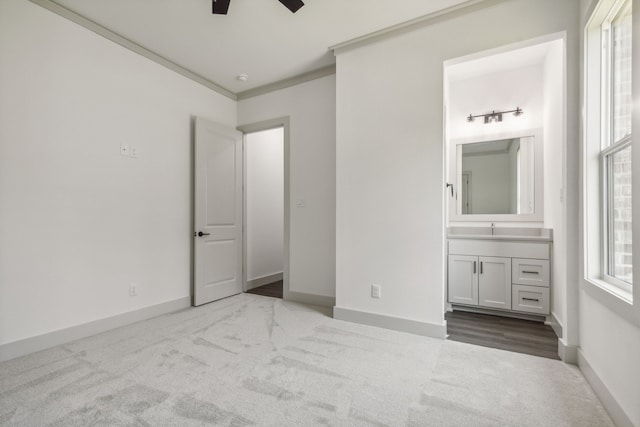 unfurnished bedroom with sink, ceiling fan, ensuite bathroom, ornamental molding, and light carpet