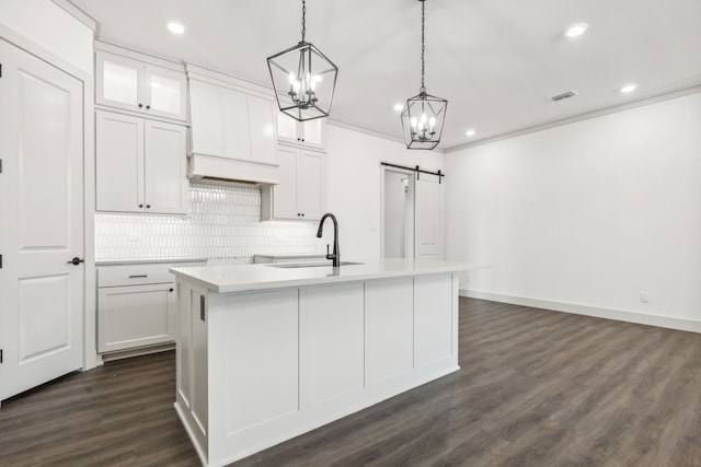 kitchen featuring a barn door, decorative light fixtures, sink, and a center island with sink