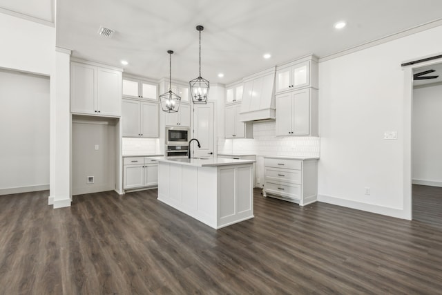 kitchen with built in microwave, an island with sink, pendant lighting, and white cabinets