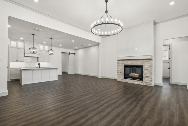 unfurnished living room featuring dark wood-type flooring, crown molding, a barn door, a notable chandelier, and a fireplace