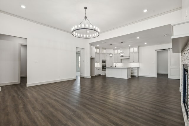 unfurnished living room featuring a chandelier, a barn door, dark hardwood / wood-style flooring, and sink