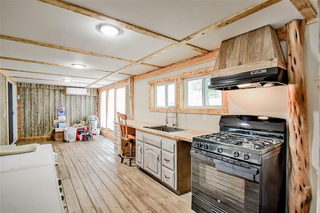 kitchen with a wall mounted AC, black gas range, light hardwood / wood-style floors, custom exhaust hood, and sink